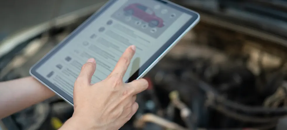 A person using a tablet to check preventative maintenance details in front of a car.