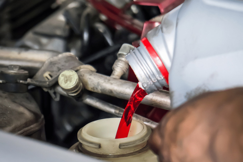 transmission fluids, auto repair in Milwaukee, WI at Next Level Auto Services. Transmission fluid service in progress. Image shows red fluid being poured into a vehicle’s transmission reservoir, highlighting the importance of regular maintenance to ensure smooth gear shifts and system reliability.