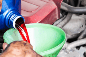 transmission fluid, auto repair in Milwaukee, WI at Next Level Auto Services. Image of red transmission fluid being poured into a vehicle through a green funnel, highlighting the shop’s focus on vehicle longevity, safety, and peak transmission performance.