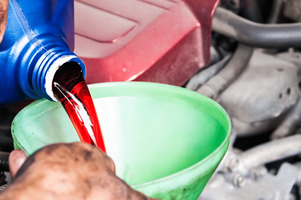 transmission fluid, auto repair in Milwaukee, WI at Next Level Auto Services. Image of red transmission fluid being poured into a vehicle through a green funnel, highlighting the shop’s focus on vehicle longevity, safety, and peak transmission performance.